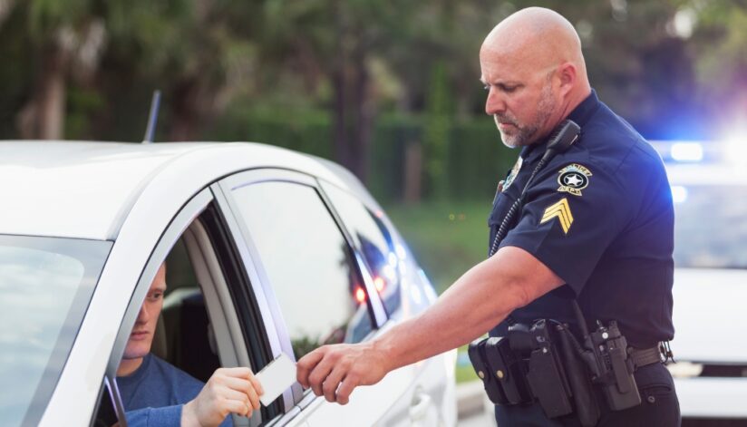 Person pulled over hands his drivers license to the police officer. Bosshard Parke traffic citations and criminal defense law.