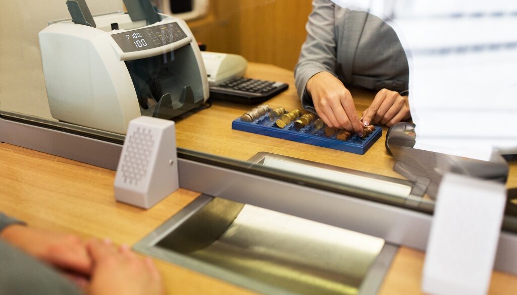 Bank teller counts money while customer sits opposite. Bosshard Parke Banking Law in La Crosse, WI.