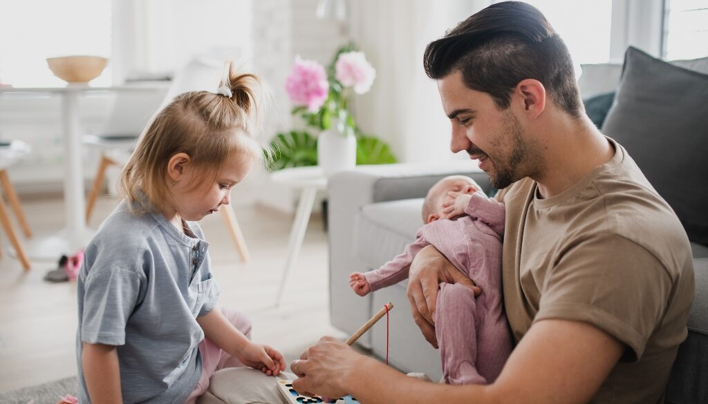 Father holds a baby and playing a game with his toddler-aged daughter. Paternity in Wisconsin law; Bosshard Parke.