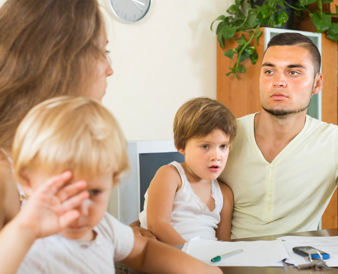 Children sit on their parents laps while the parents argue. Man looks shocked. Divorce and Family Law at Bosshard Parke in La Crosse, WI.