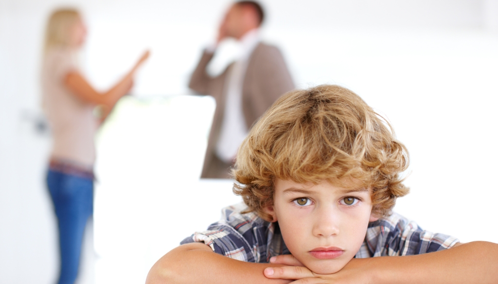 Child looking sad while parents argue behind him.