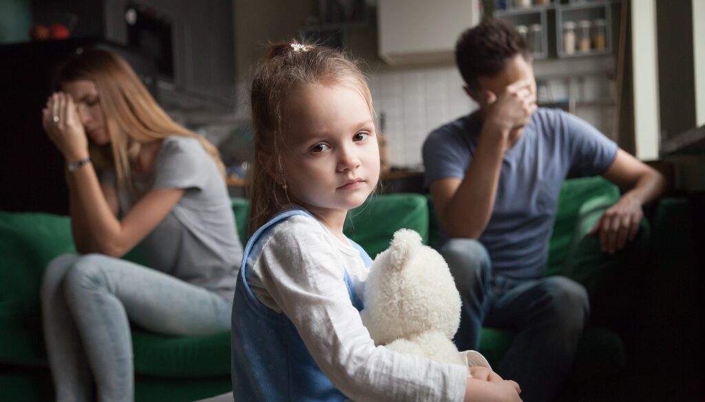 Child looking sad while parents sit away from each other in the background.