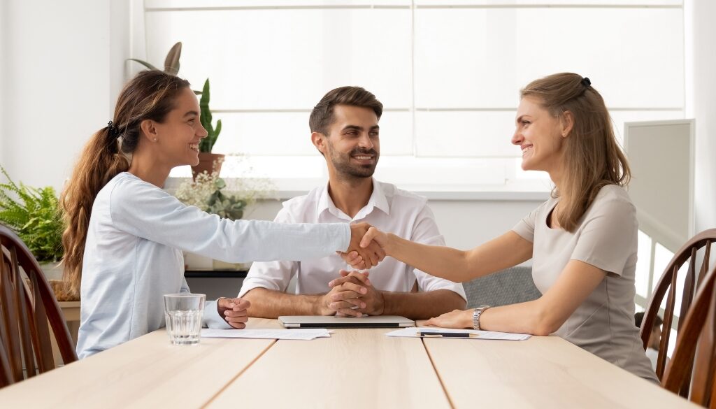 Two women utilizing family mediation, shaking hands, and smiling.