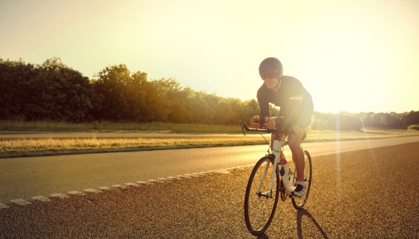 A bicyclist riding on the road with the sun shining behind him.