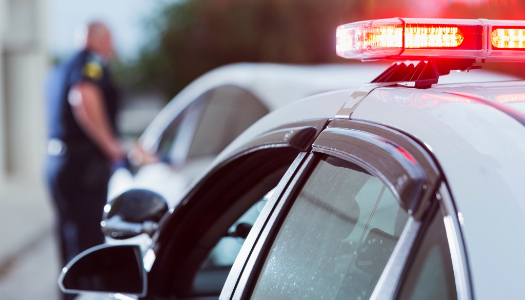 A cop car with its lights on and an officer in the distance performing a traffic stop.