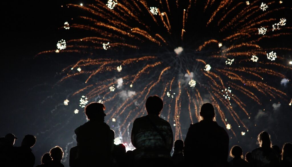 Silhouettes of people looking up at a firework on the 4th of July.