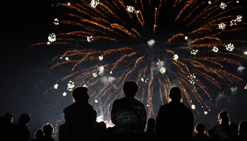 Silhouettes of people looking up at a firework on the 4th of July.