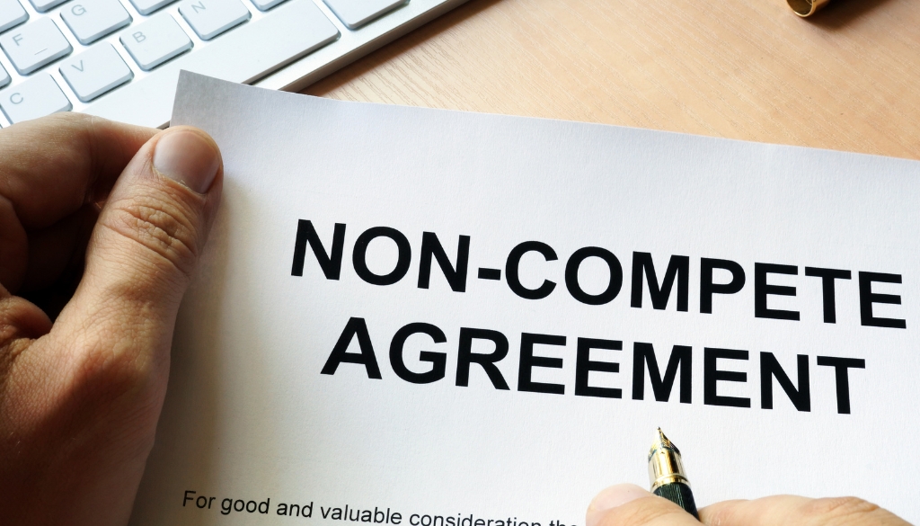 A person holding a pen and non-compete agreement.