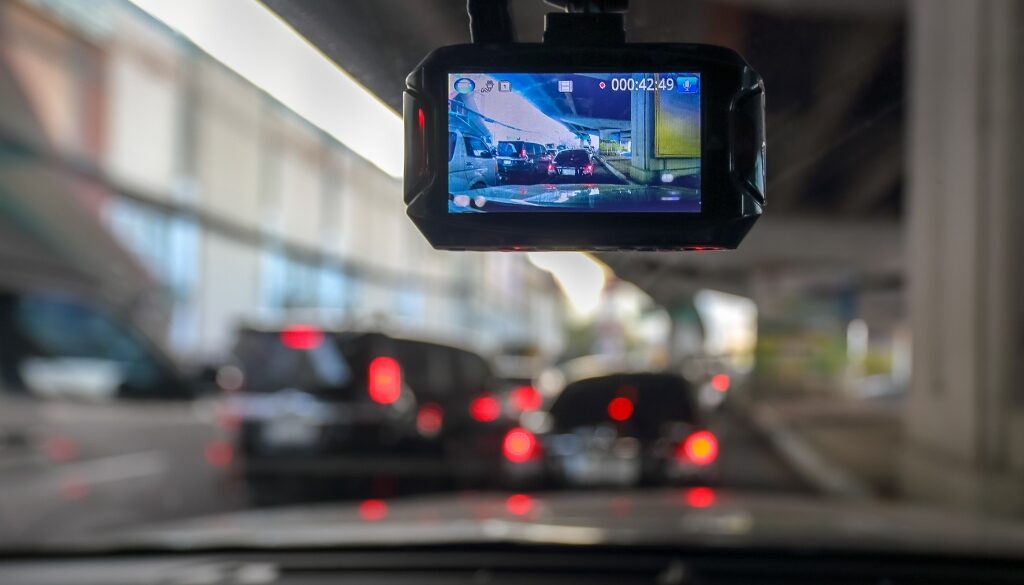 View of a road through a dashcam screen mounted in a car, showing other vehicles on a congested highway.