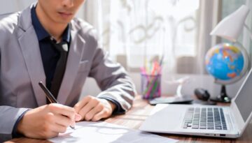 College aged man signing a document next to a laptop.