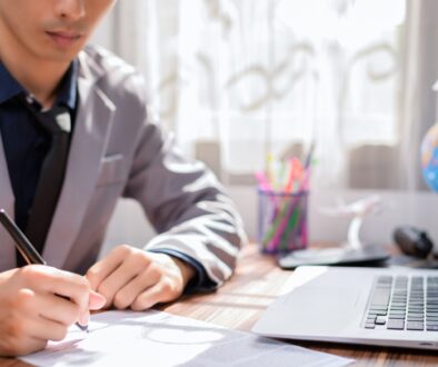 College aged man signing a document next to a laptop.