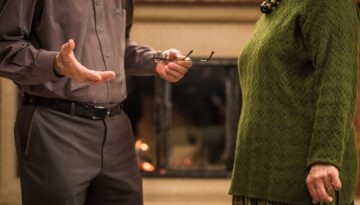 An older couple engaged in a serious discussion in front of a fireplace.