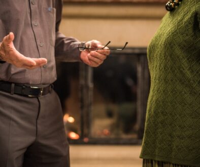 An older couple engaged in a serious discussion in front of a fireplace.