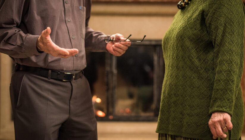 An older couple engaged in a serious discussion in front of a fireplace.