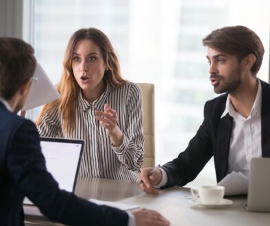 Three employees sitting around a conference table in a heated argument at the office.