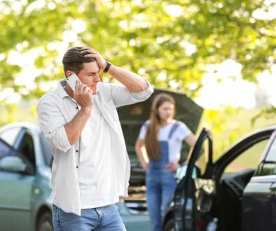 Man on the phone after a car accident with a woman and two damaged vehicles in the background.