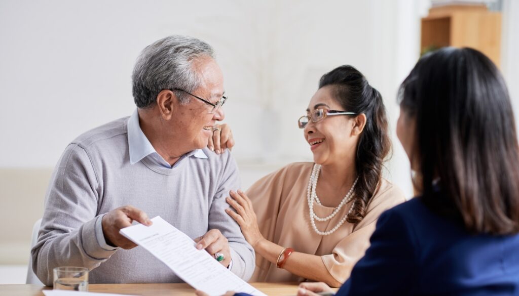 An elderly couple smiling while discussing estate planning documents with an attorney.