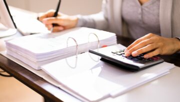 Close-up of a business professional reviewing financial documents with a calculator, preparing for an IRS audit in a well-organized workspace.