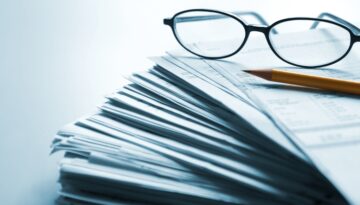 Stack of documents with eyeglasses and a pencil on top.