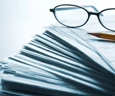 Stack of documents with eyeglasses and a pencil on top.