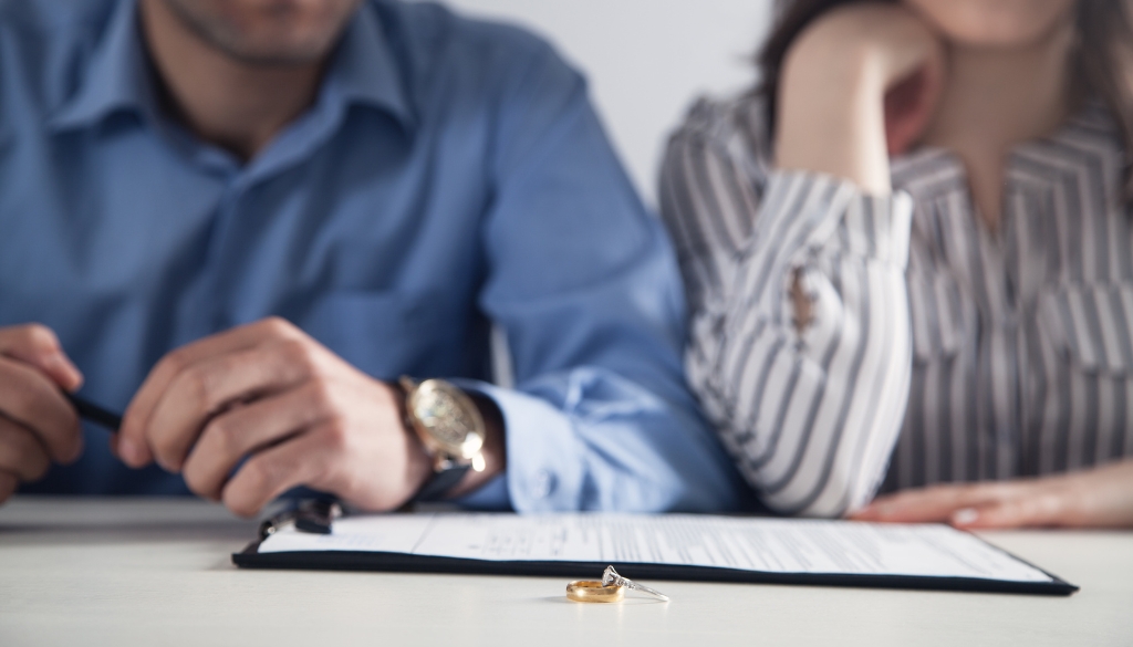 A couple reviewing divorce paperwork at a table with a wedding ring placed on the document.