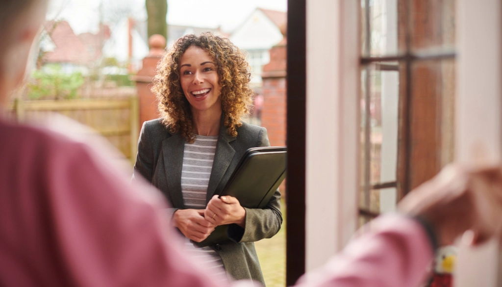 A professional landlord meeting a tenant at the door of a residential property, holding a folder and smiling warmly.