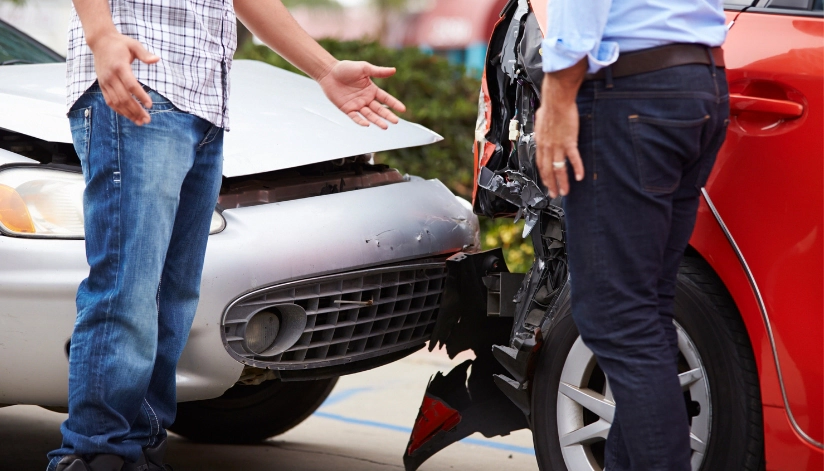 Two men standing next to damaged cars after a collision, gesturing and discussing the accident.