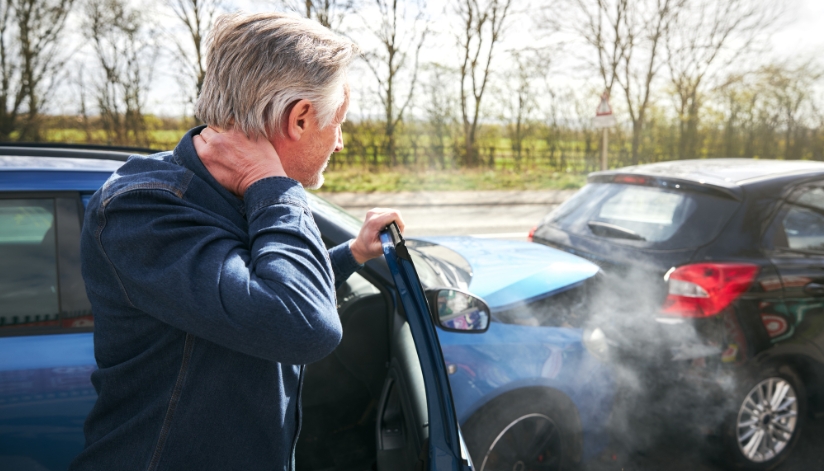 Common Mistakes After A Car Accident That Could Hurt Your Injury Claim Man holding his neck in pain after a rear-end car accident, standing next to his vehicle with visible collision damage and smoke.