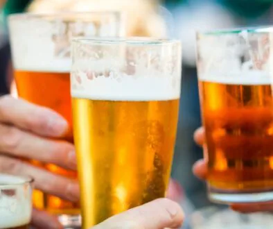 Close-up of people clinking glasses of beer at an outdoor gathering.