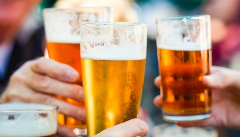 Close-up of people clinking glasses of beer at an outdoor gathering.