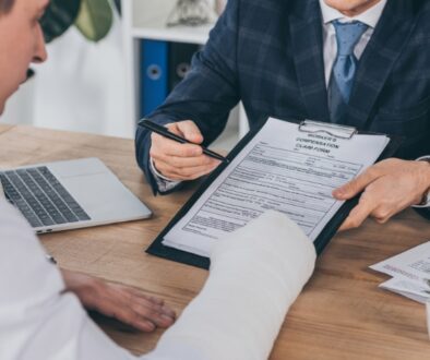 Injured worker with a bandaged arm discussing a workers' compensation claim form with an attorney in a professional office setting.