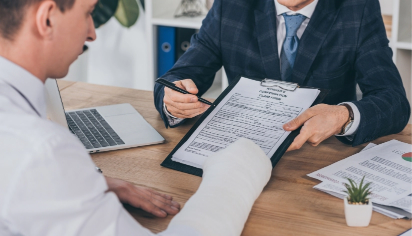 How Long After a Workplace Injury Can You File For Workers’ Compensation In Wisconsin? Injured worker with a bandaged arm discussing a workers' compensation claim form with an attorney in a professional office setting.