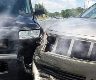 Two vehicles with front-end damage after a car accident on a Wisconsin roadway, with smoke rising from both hoods.