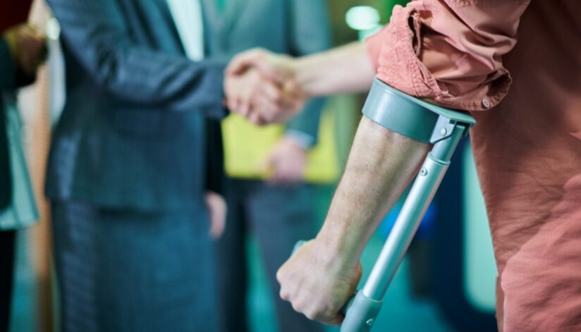 Close up of an injured worker using crutches shaking hands with a professional.