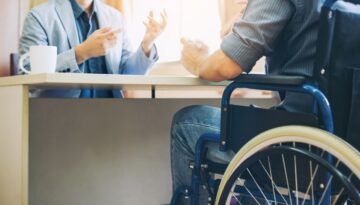 A man in a wheelchair speaks with an attorney across a desk in an office, discussing a long term disability claim.