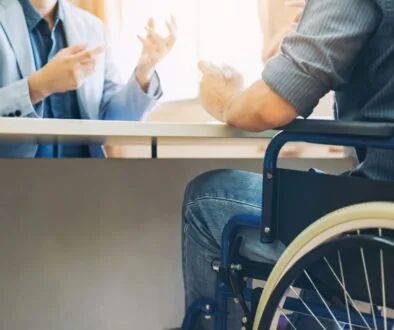 A man in a wheelchair speaks with an attorney across a desk in an office, discussing a long term disability claim.
