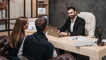 A newly engaged couple sitting across from a professional attorney in an office, and discussing a prenuptial agreement.