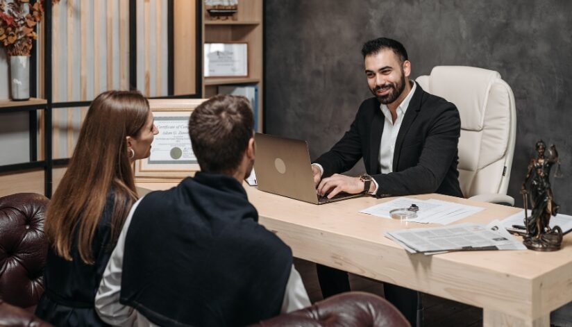 A newly engaged couple sitting across from a professional attorney in an office, and discussing a prenuptial agreement.