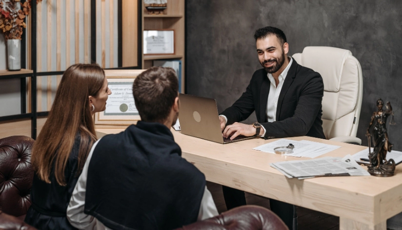 A newly engaged couple sitting across from a professional attorney in an office, and discussing a prenuptial agreement.