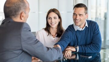 A smiling couple meets with an attorney during an initial consultation, shaking hands across a desk.
