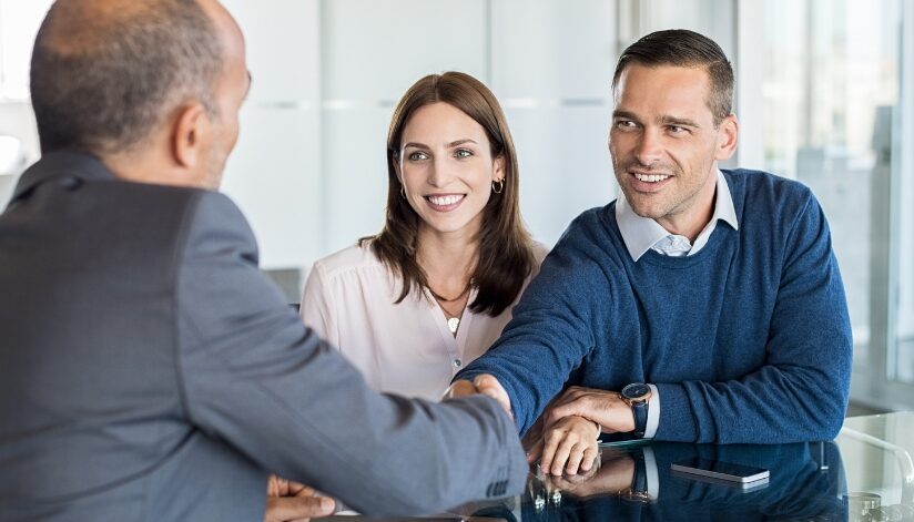 A smiling couple meets with an attorney during an initial consultation, shaking hands across a desk.