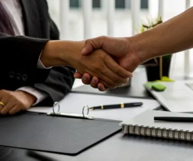 A business law attorney and client shake hands across a desk after finalizing legal or contract discussions in a professional office setting.