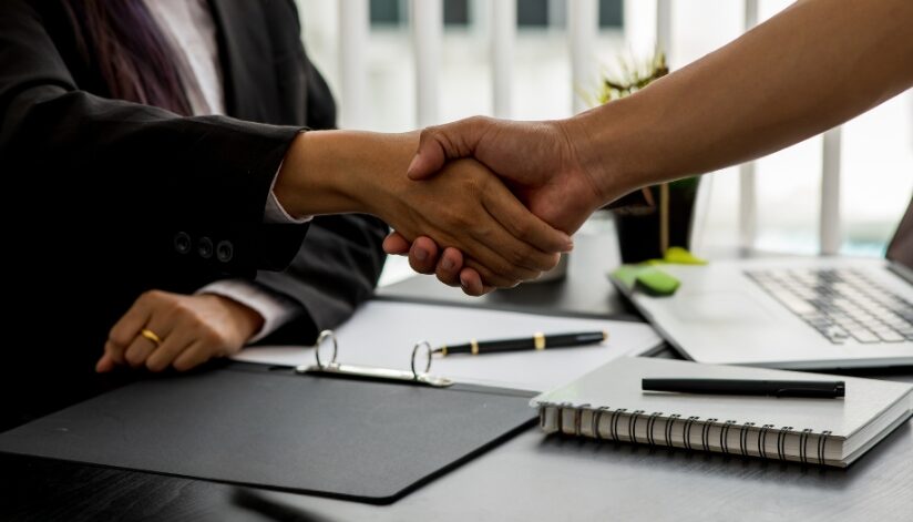 A business law attorney and client shake hands across a desk after finalizing legal or contract discussions in a professional office setting.