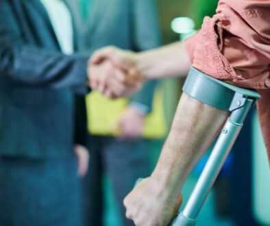 A personal injury attorney shakes hands with a client using crutches after discussing a long-term injury case and compensation options.