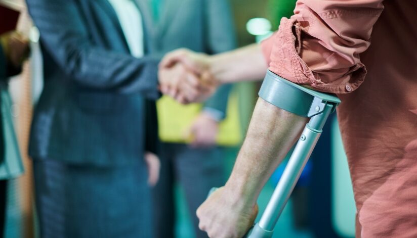 A personal injury attorney shakes hands with a client using crutches after discussing a long-term injury case and compensation options.
