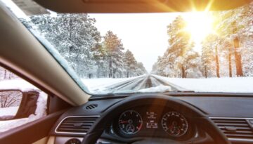 The view of the inside of a car driving down a snowy road surrounded by pine trees in Wisconsin.