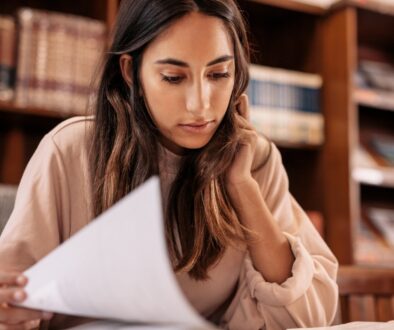 A college-aged woman sitting in a library reviewing paperwork