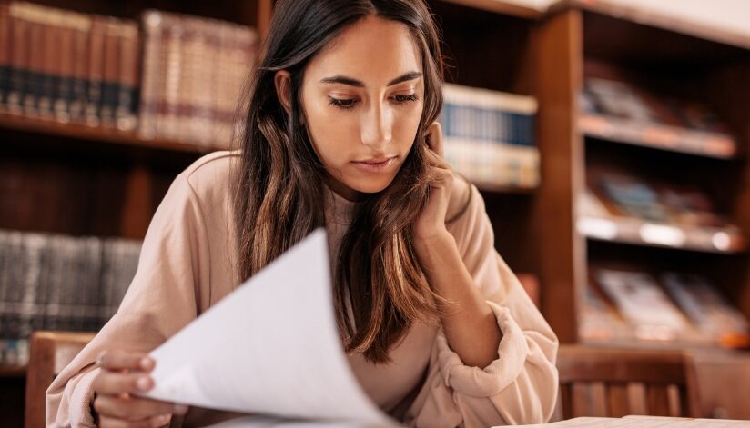 A college-aged woman sitting in a library reviewing paperwork