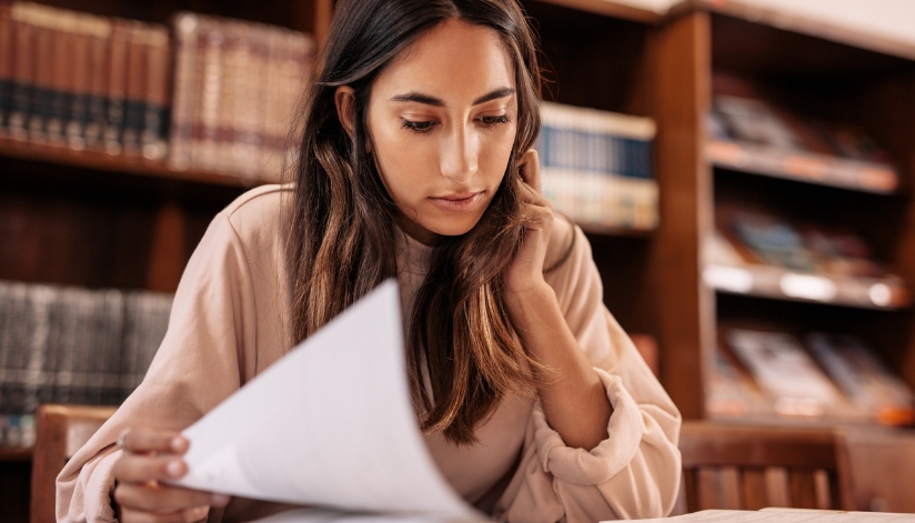 A college-aged woman sitting in a library reviewing paperwork