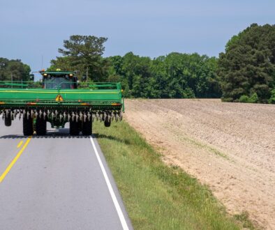Wide farm tractor traveling on a rural Wisconsin road beside a field.